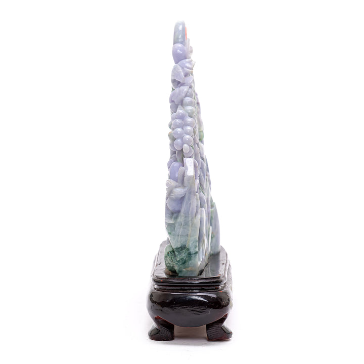 Intricate jade artwork of geese frolicking by a brick house surrounded by grape foliage.