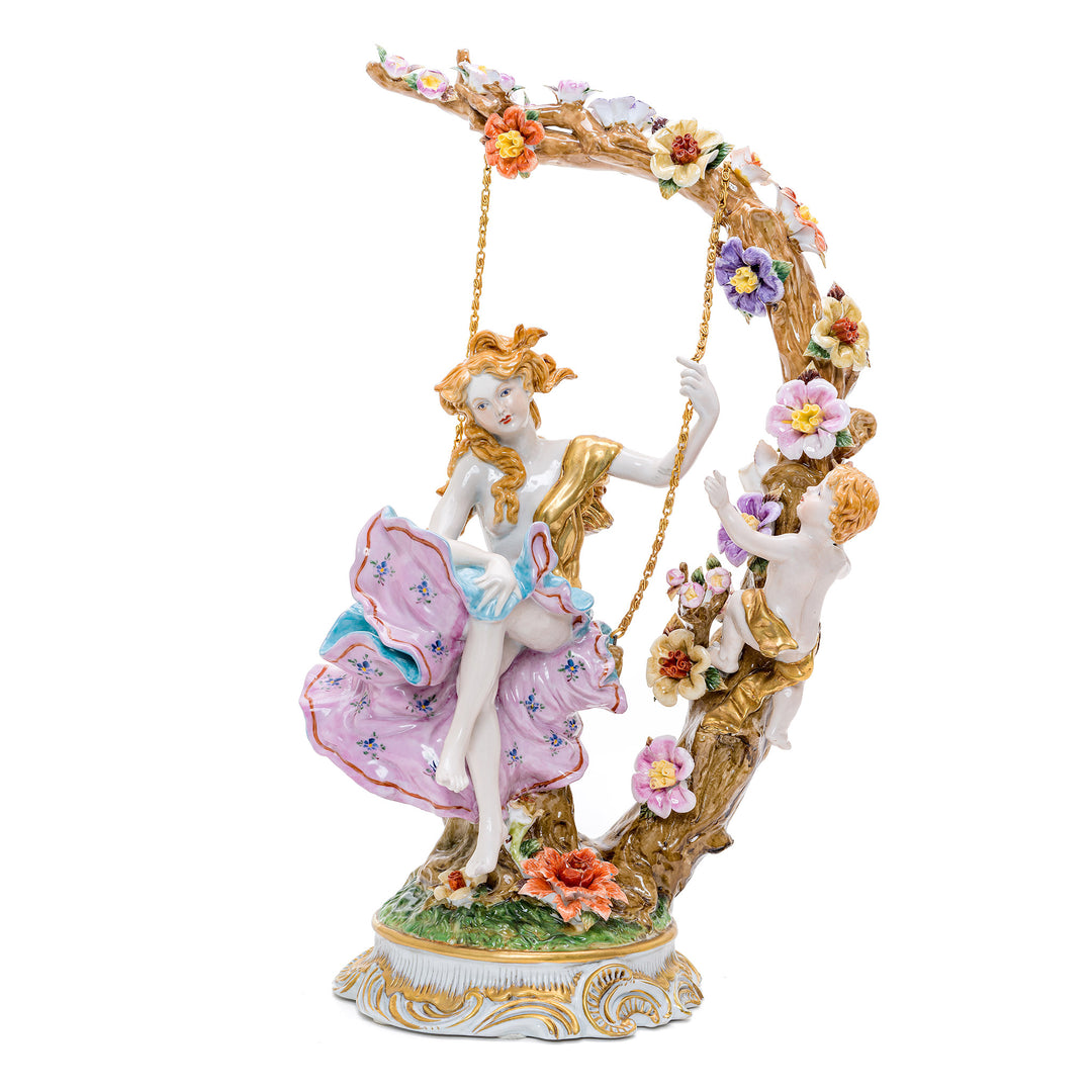 Handmade porcelain sculpture of a young woman on a tree swing with a cherub.