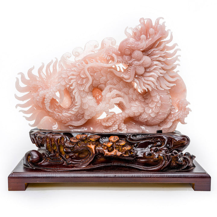 Hand-carved writhing dragon sculpture in rose quartz on a wooden base.