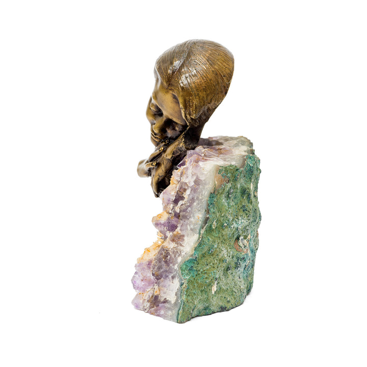 Side view of peaceful bronze head resting atop purple crystal