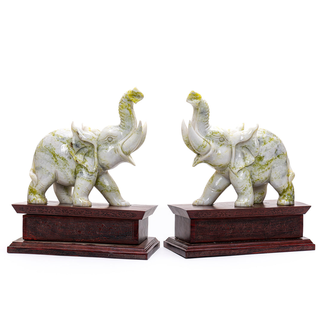 Handcrafted elephant statuettes with spinach green accents on wooden pedestals.