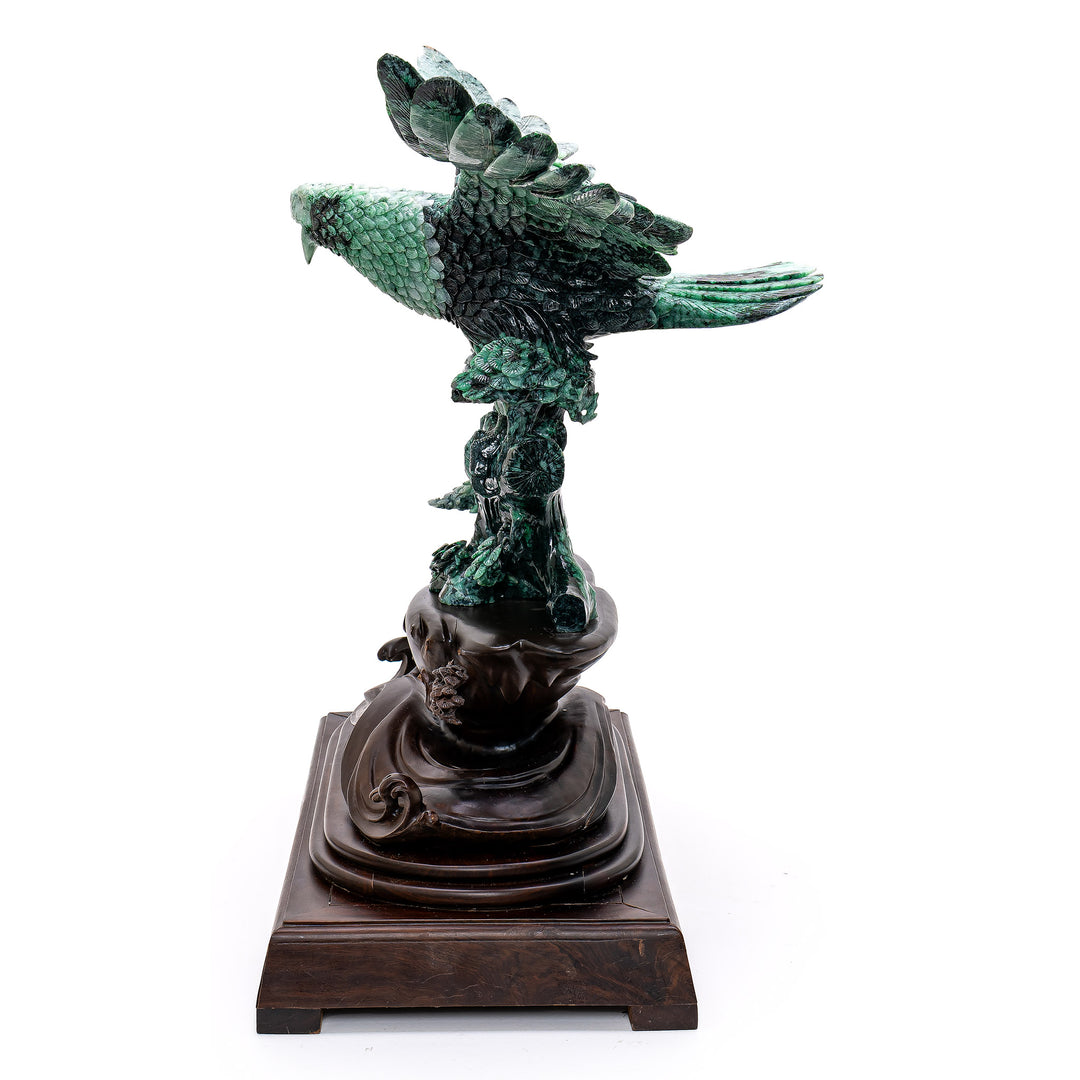 Intricate jade carving of a powerful eagle atop vibrant foliage.