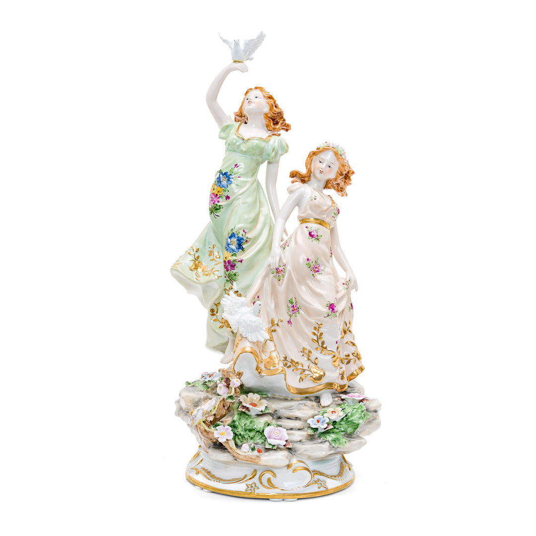 Handmade porcelain sculpture of two women with doves in a serene garden.