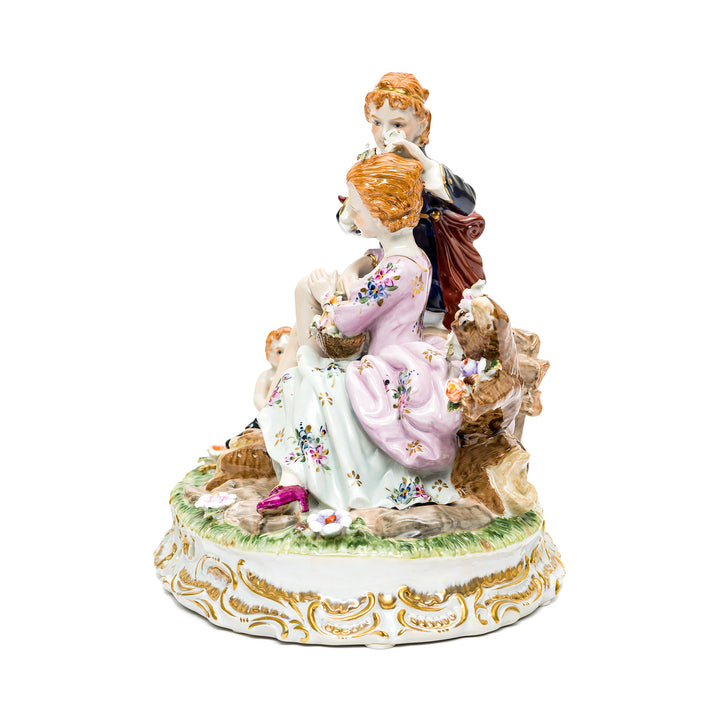 Elegant porcelain couple and cherub statue on ornate base.